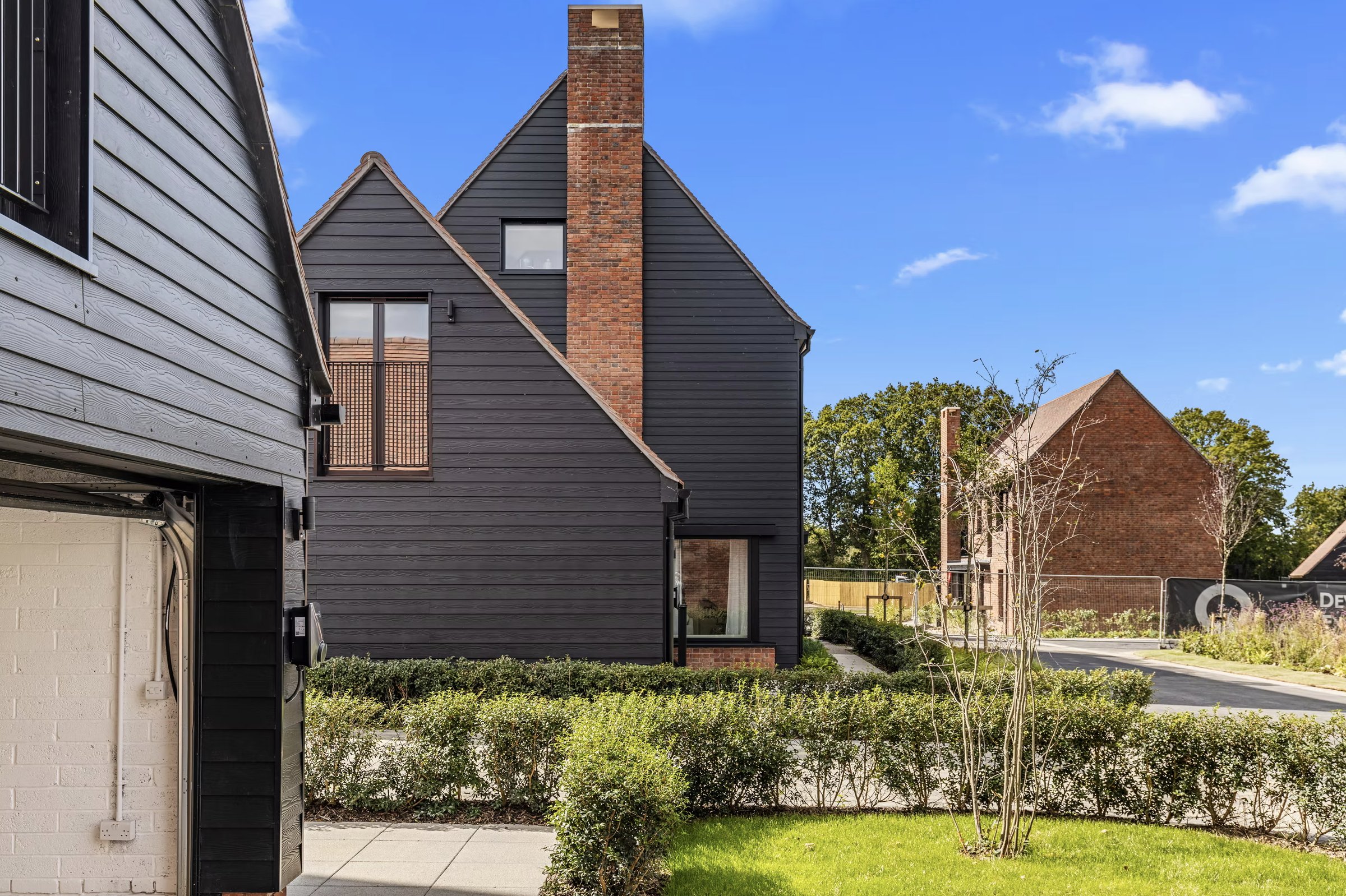Alfold Gardens exterior detail with dark timber cladding and brick chimney — Surrey development by Ademchic