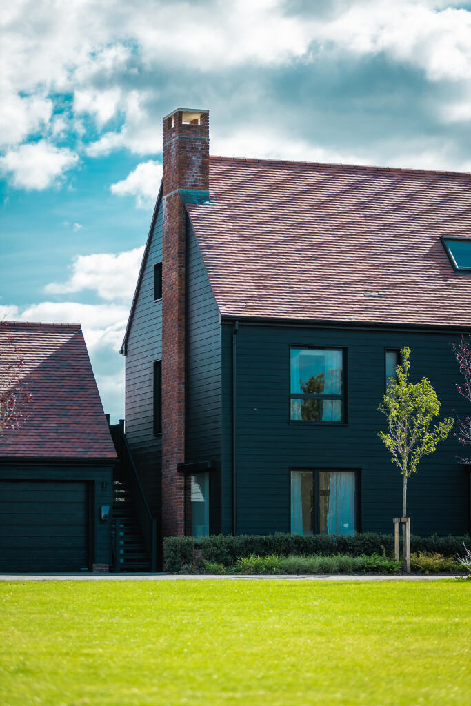 Alfold Gardens dramatic view of dark timber cladding with brick chimney — Surrey development by Ademchic